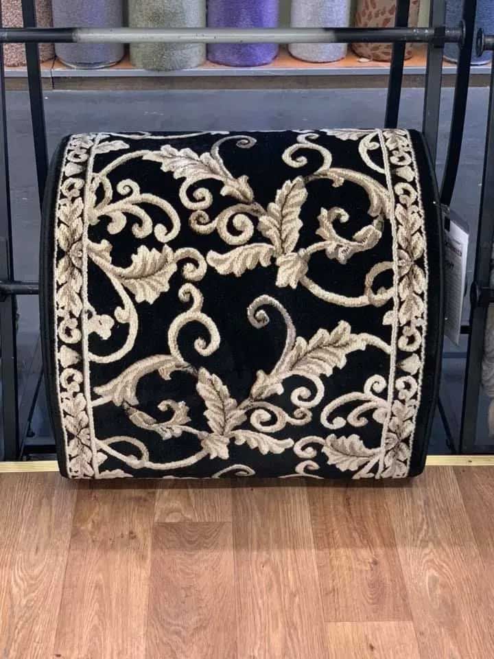 Black lumbar support cushion with beige floral design, on wooden floor.