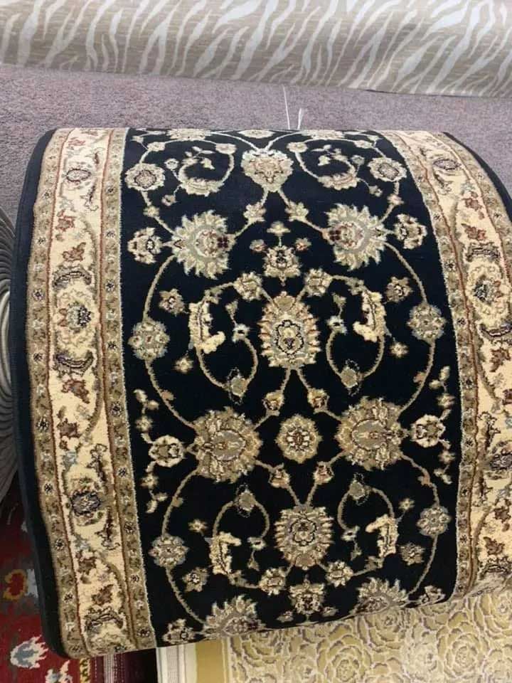 Rolled black rug with beige floral pattern and border, in a carpet store.
