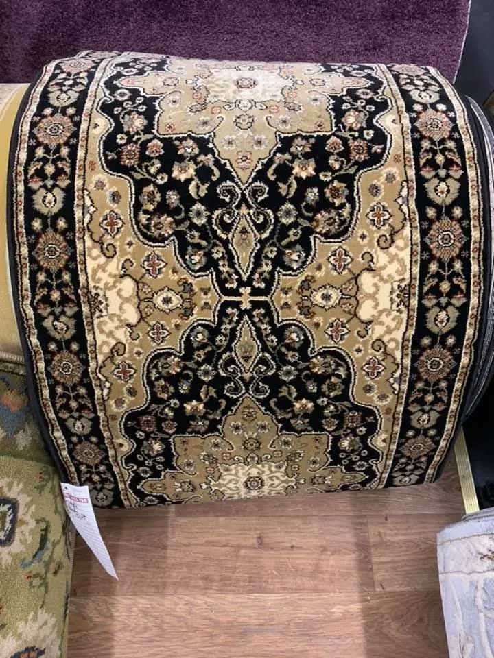 Rolled-up beige and black patterned carpet on a wooden floor.