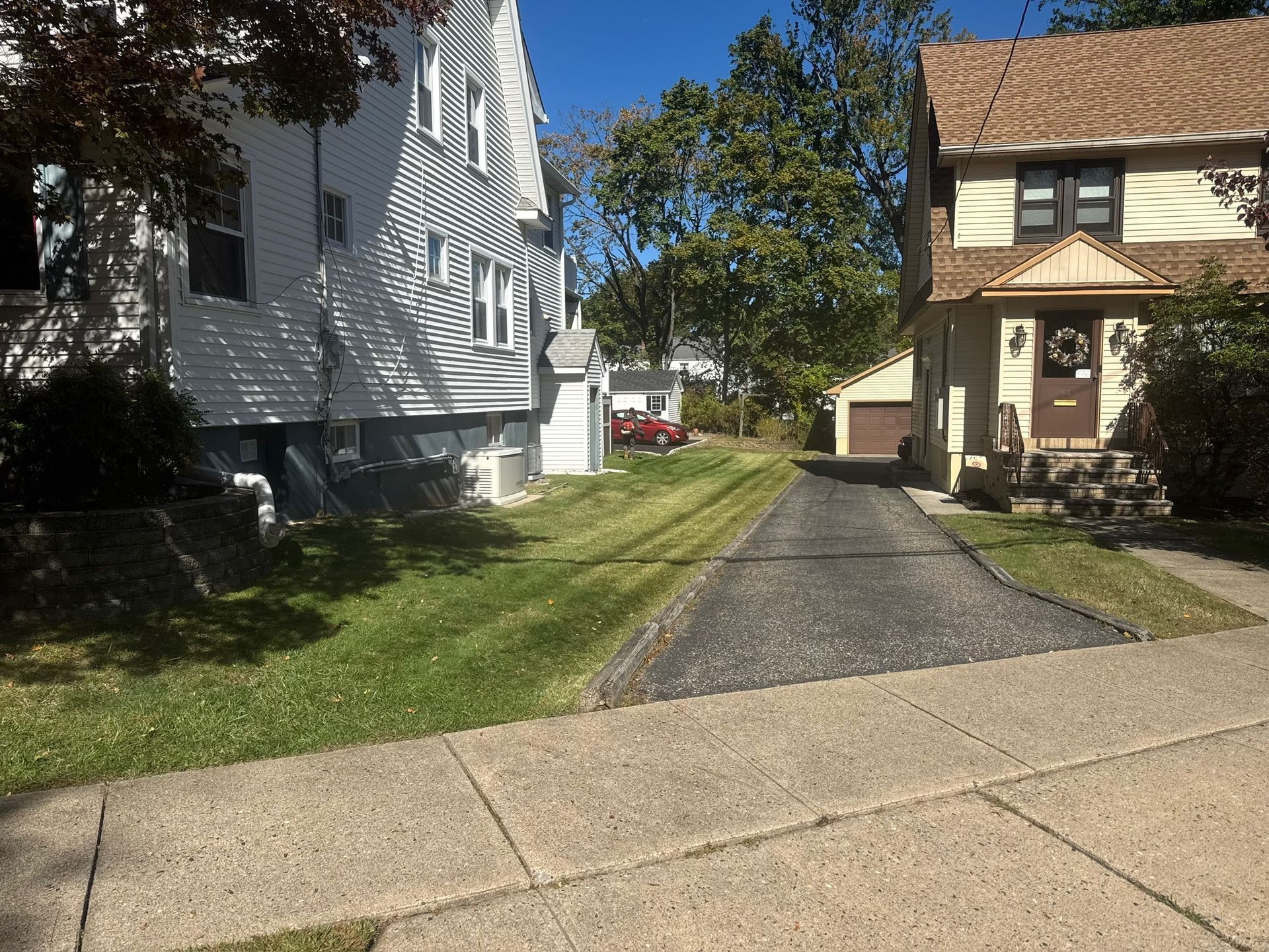 Residential street scene: houses, driveway, sidewalk, lawn, sunny day.