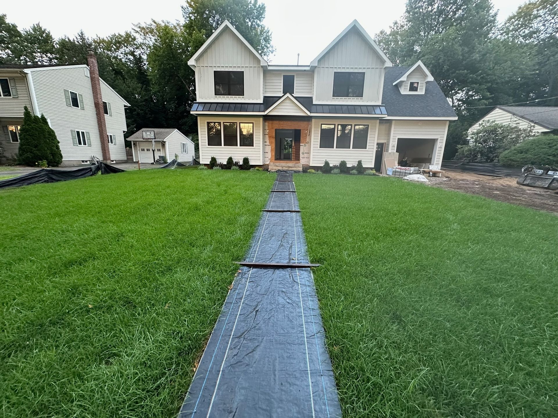 Two-story beige house with a brown front door, a path through the green lawn, and a garage.