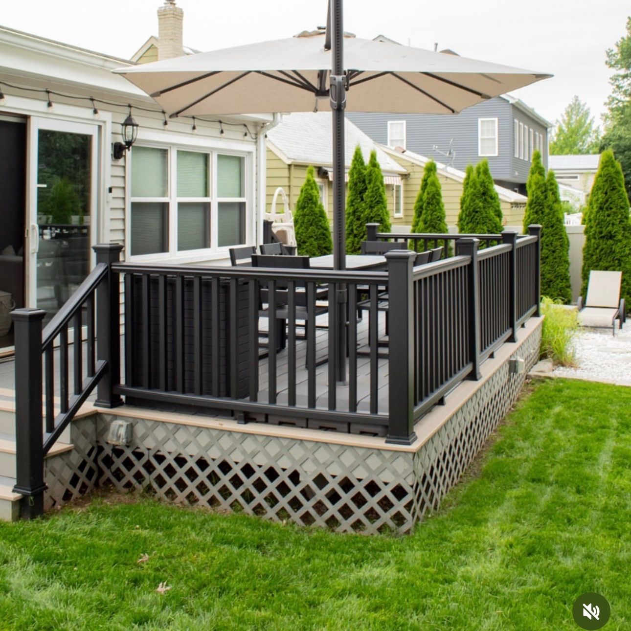 Black deck with matching railing and an umbrella over outdoor dining furniture. Green lawn.