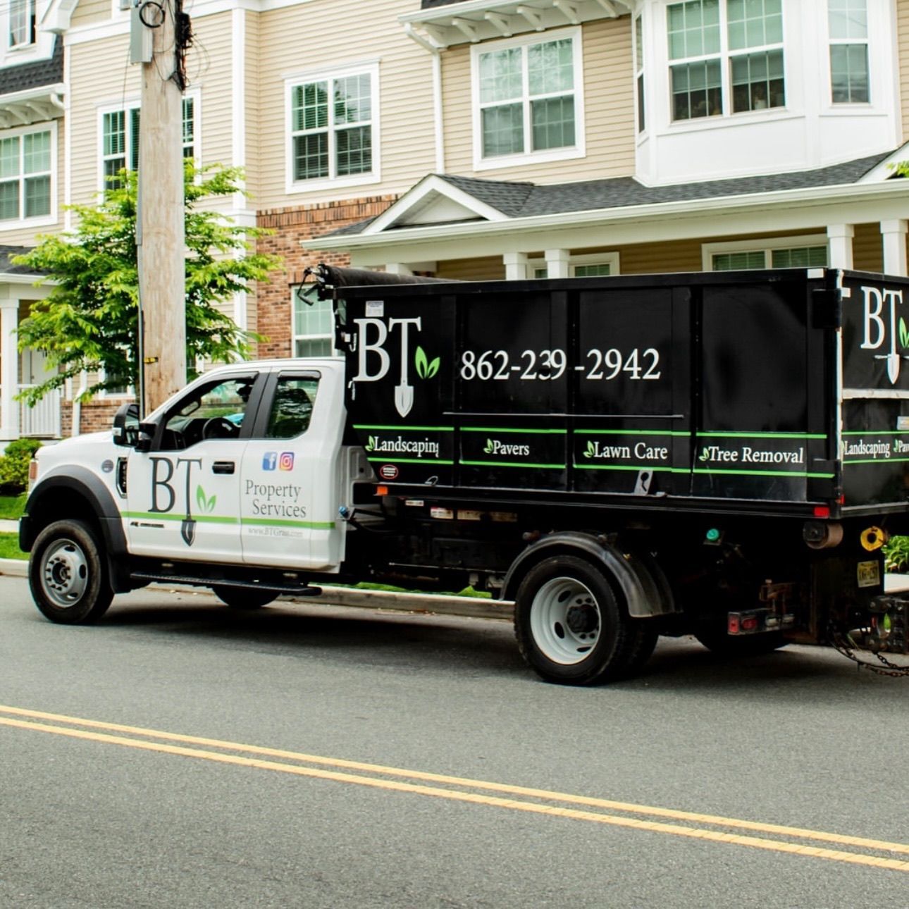 White work truck with black dumpster parked on street; company logo and phone number visible.
