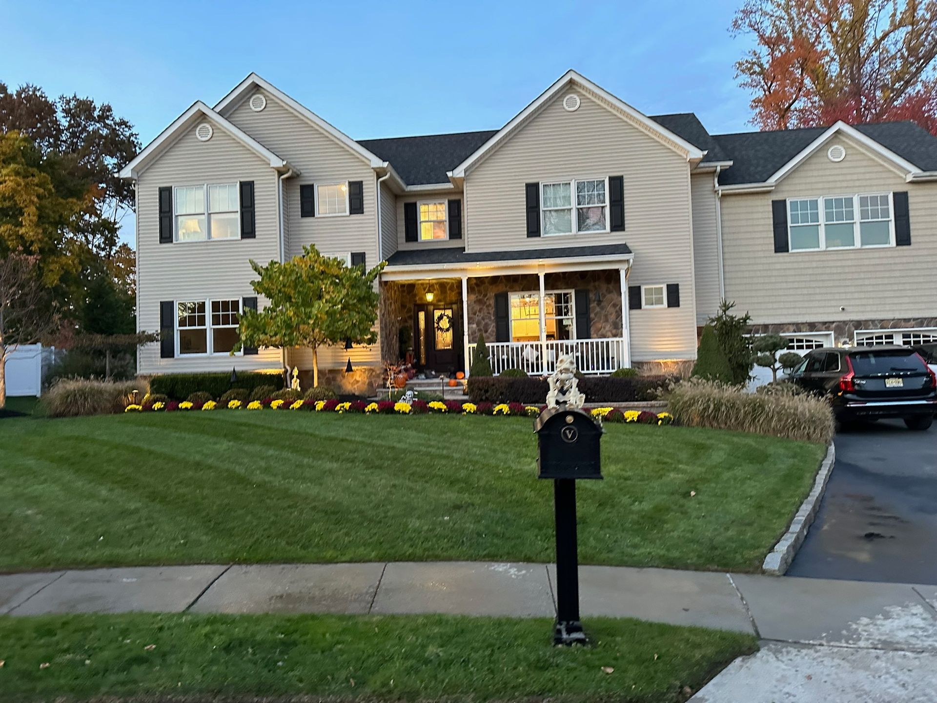 Two-story beige house with black shutters, well-manicured lawn, and a black mailbox.