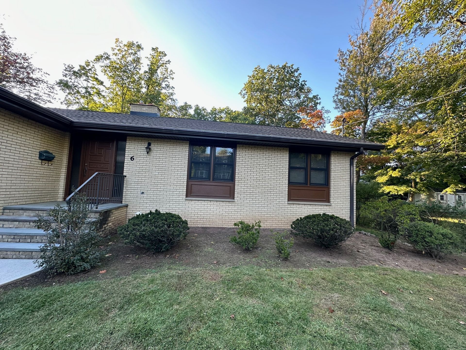 Tan brick ranch house with dark trim, windows, and roof; green lawn and shrubs in front.