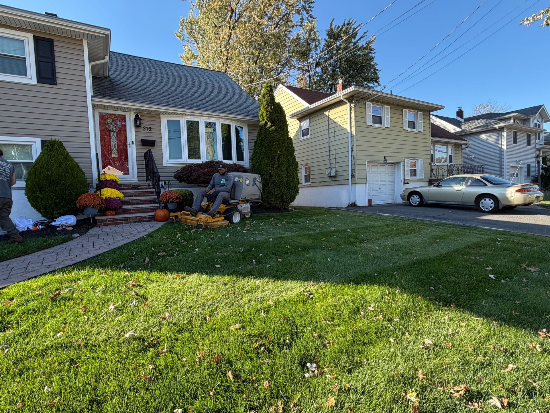 House decorated for fall with pumpkins and lawn decorations. A car is parked on the street.