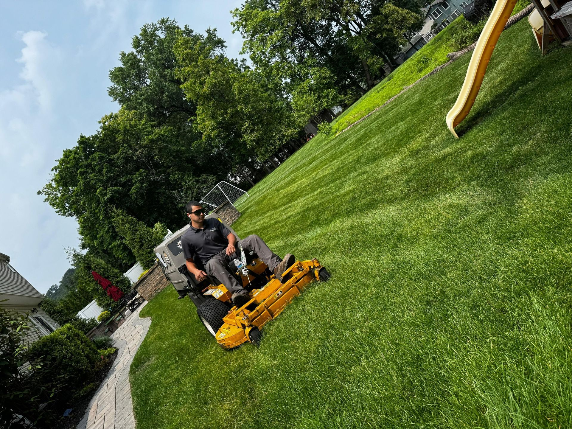 Man on riding lawnmower cutting grass on a sloped lawn in front of a house.