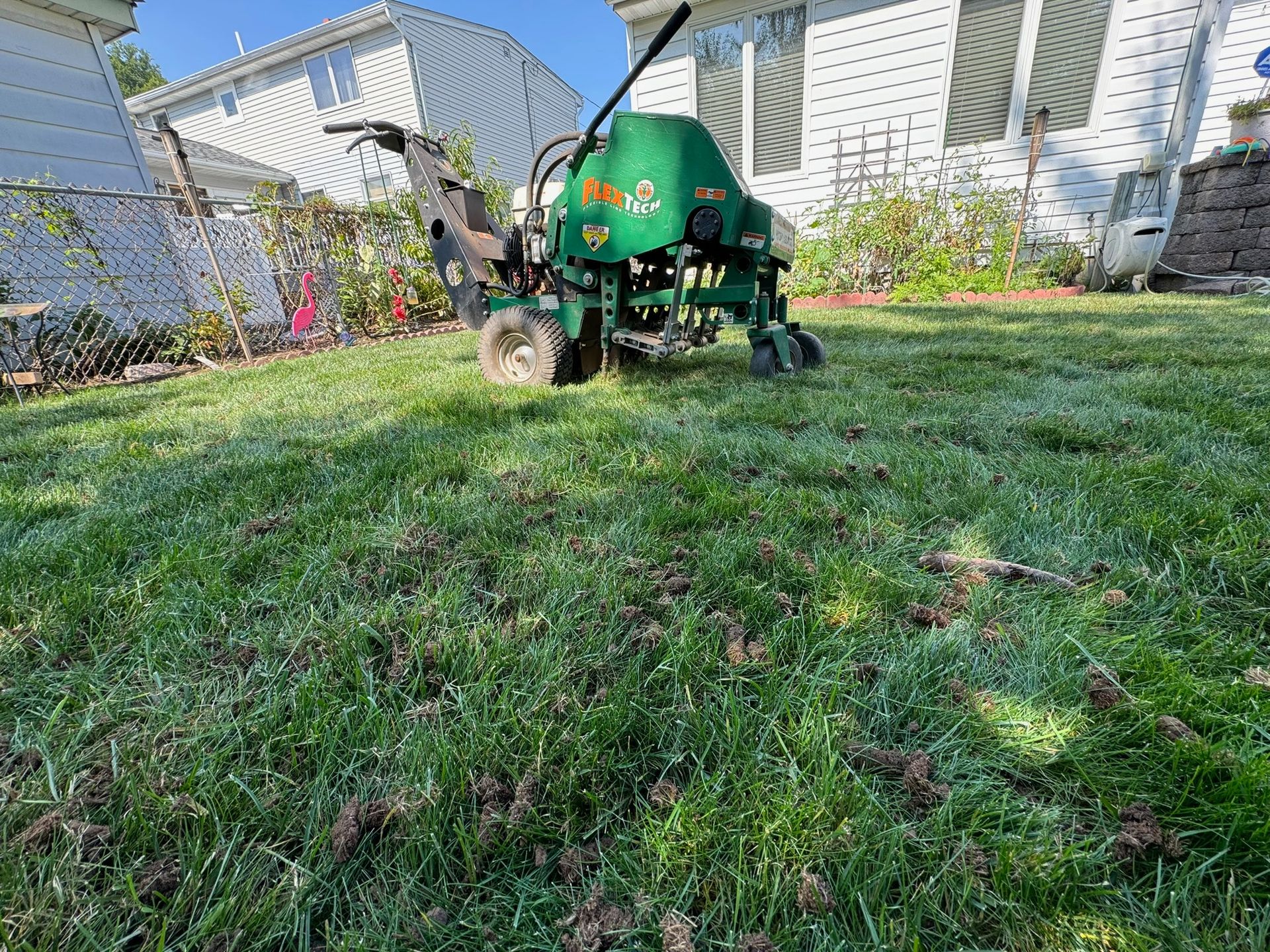 A green lawn aerator on a grass yard, creating holes. A white house is in the background.