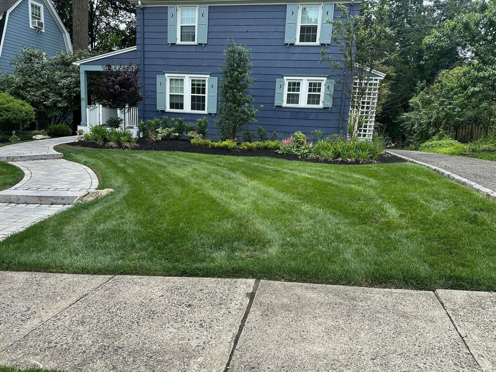 Blue house with manicured green lawn, stone walkway, and small garden.