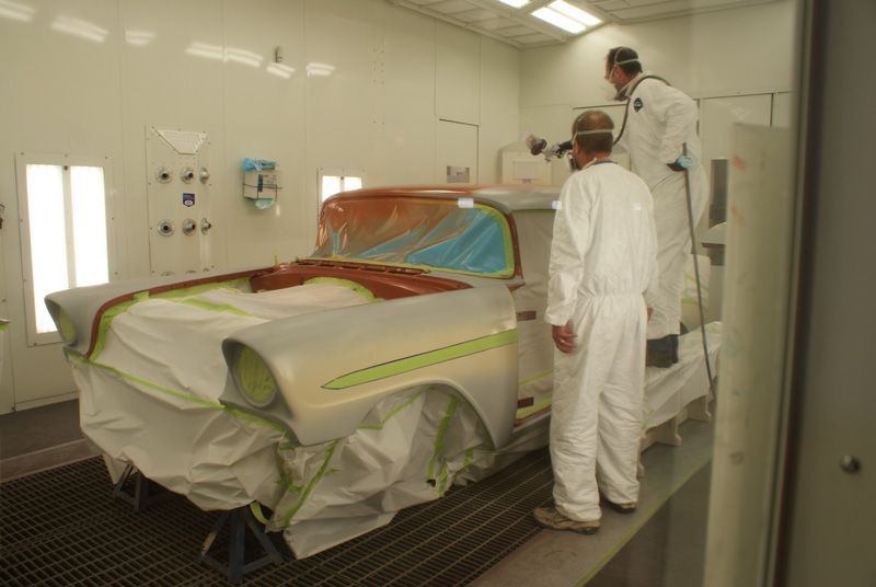 Two men are painting a car in a paint booth.