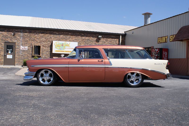 A brown and white car is parked in front of a paint shop