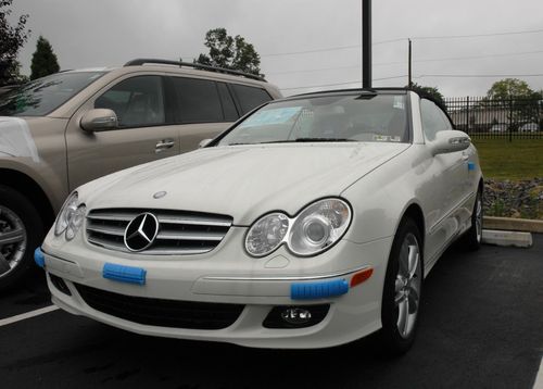White Mercedes convertible parked in a lot beside a tan SUV on a wet day