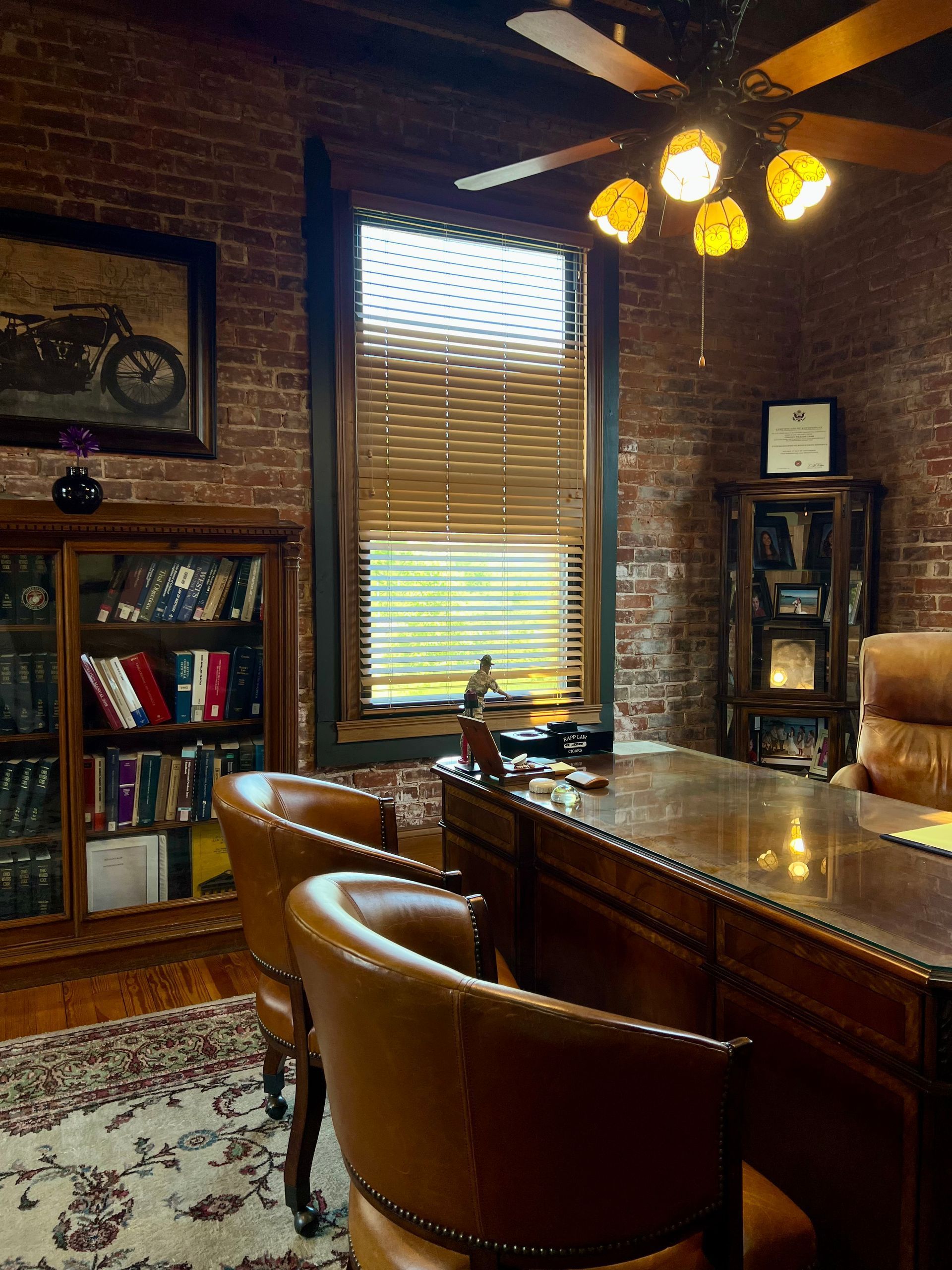 Cozy brick-walled office with leather chairs, wooden desk, bookshelves, and a window with blinds