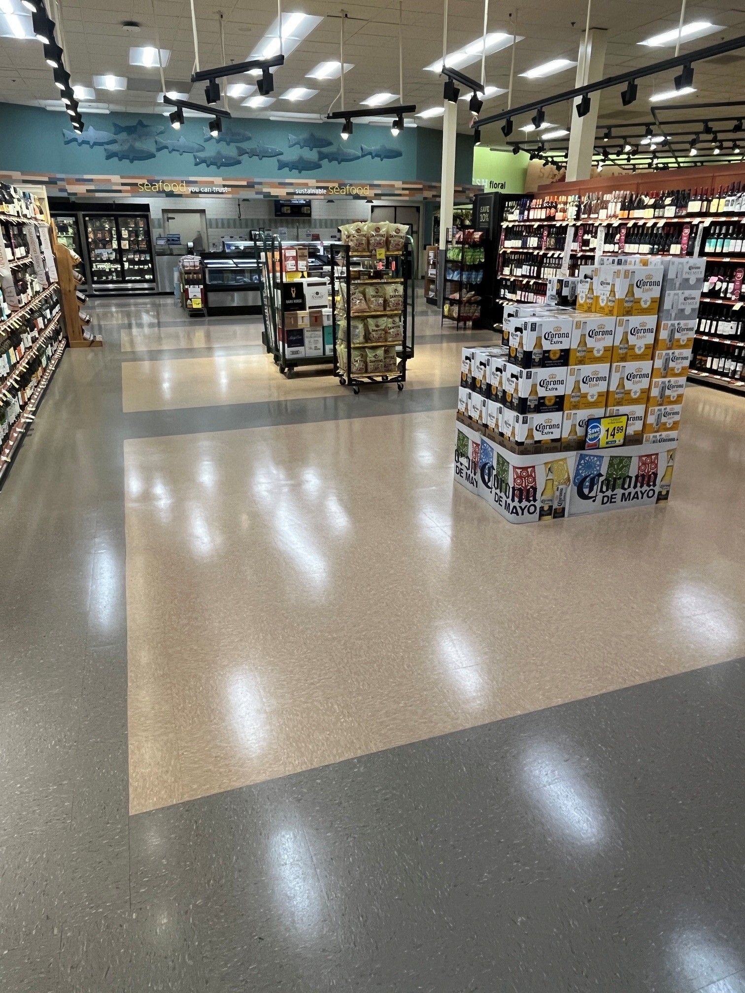 Empty grocery store aisle with bright lights, polished floor, and shelves of packaged goods and drinks.