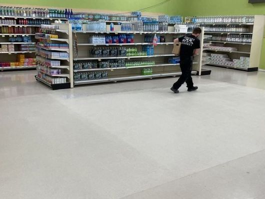 Person walking in a store aisle past shelves of toiletries and household products