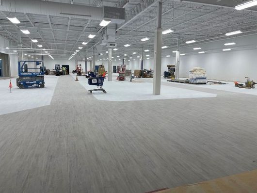 Large empty warehouse interior with concrete floor, white walls, and a few forklifts and equipment in the distance