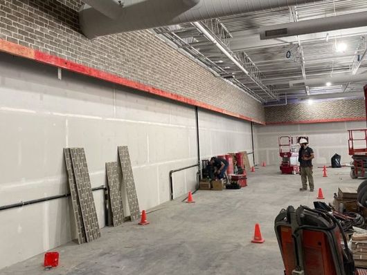 Interior construction site with workers, orange cones, tools, and ladder against a long wall