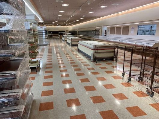 Empty grocery store aisle with shelves, carts, and orange-and-white tiled floor