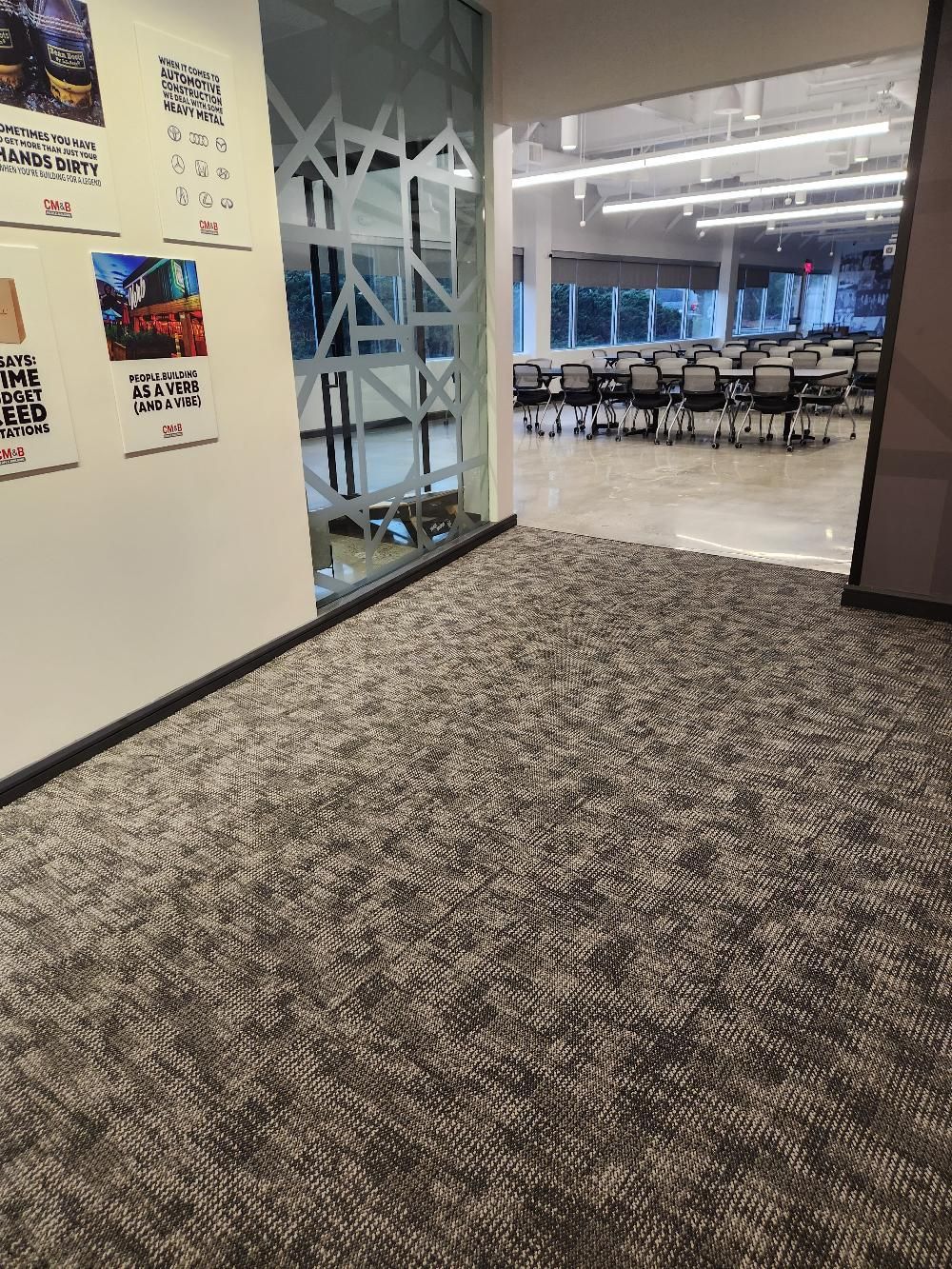 A hallway with a carpeted floor and a glass door leading to a conference room.