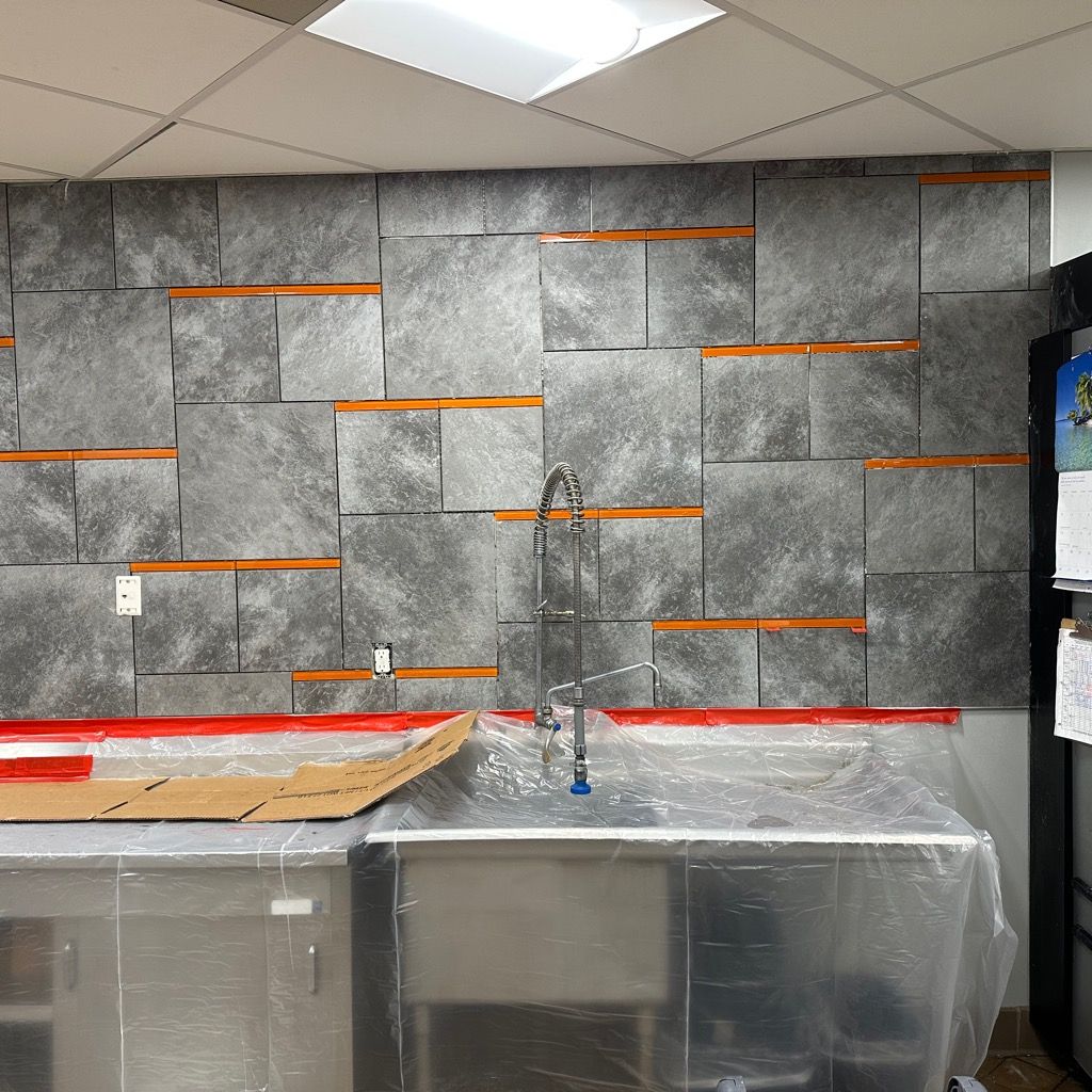 A kitchen with a gray tiled wall and a sink.