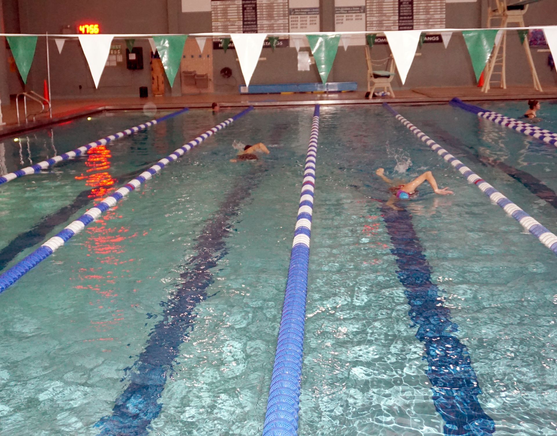 Indoor swimming pool with swimmers. Blue and white lane markers, white and green pennants.
