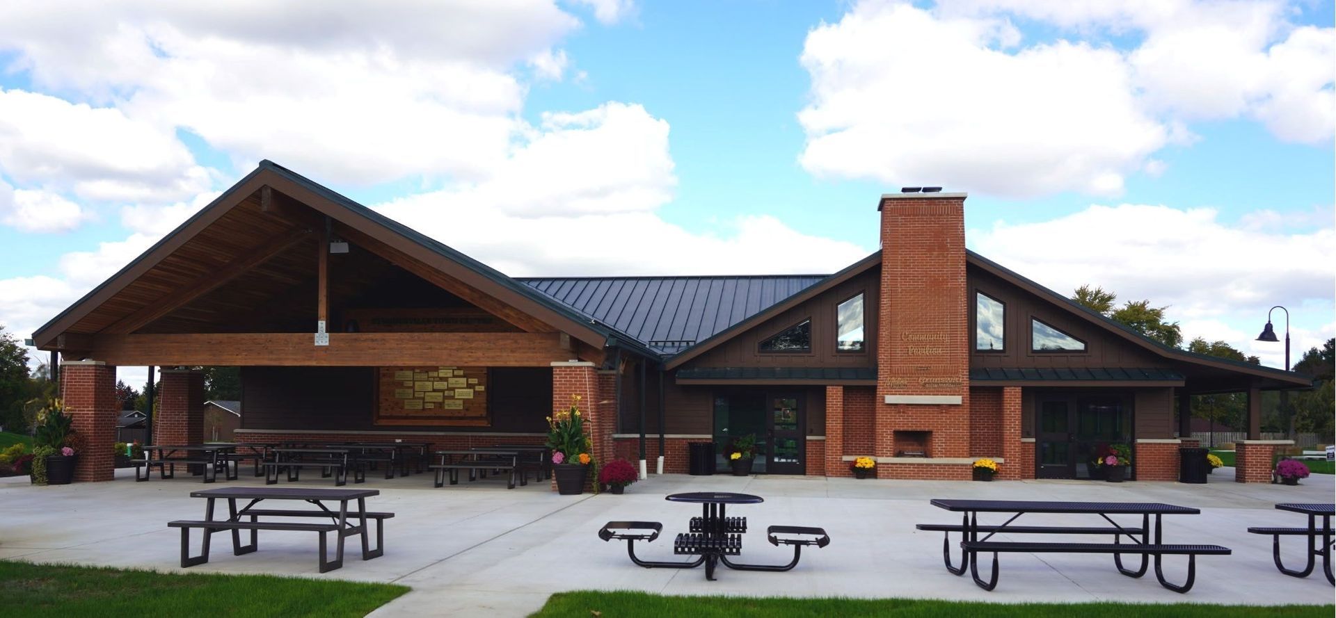Exterior view of a brick building with a covered patio, picnic tables, and a red-brick chimney.