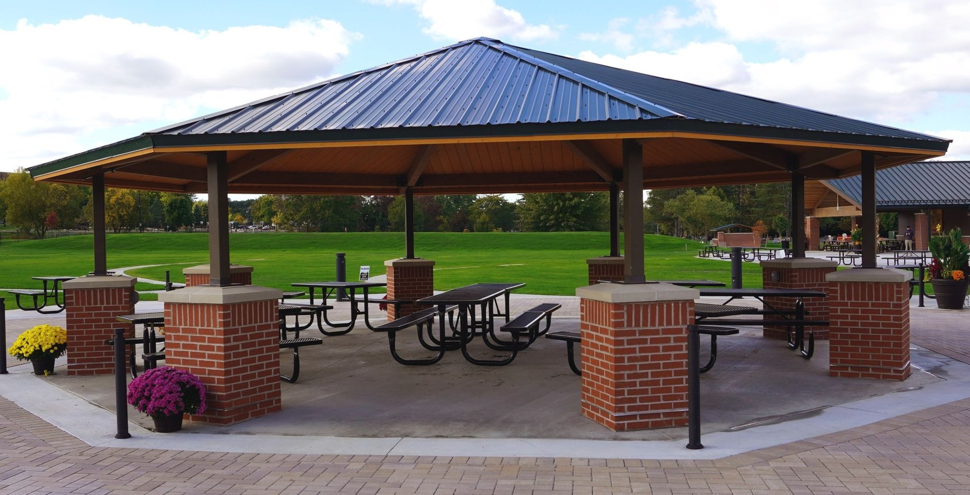 Picnic shelter with tables, brick columns, and a metal roof in a park setting.