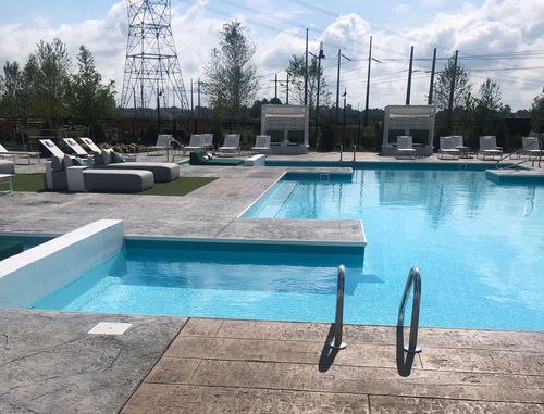 Swimming pool with lounge chairs, cabanas, and a power line in the background on a sunny day.