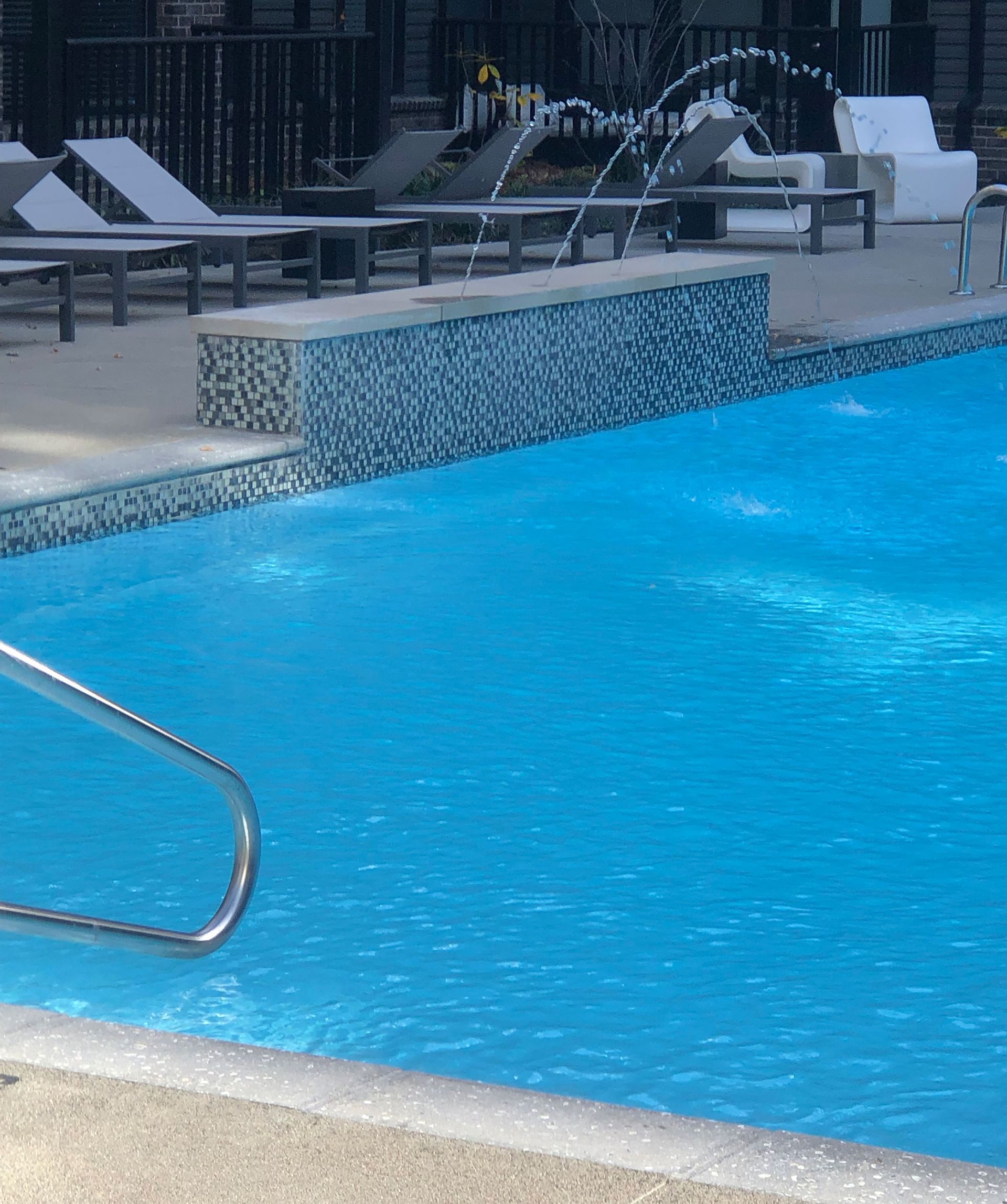 Swimming pool with water jets, lounge chairs, and tiled wall.