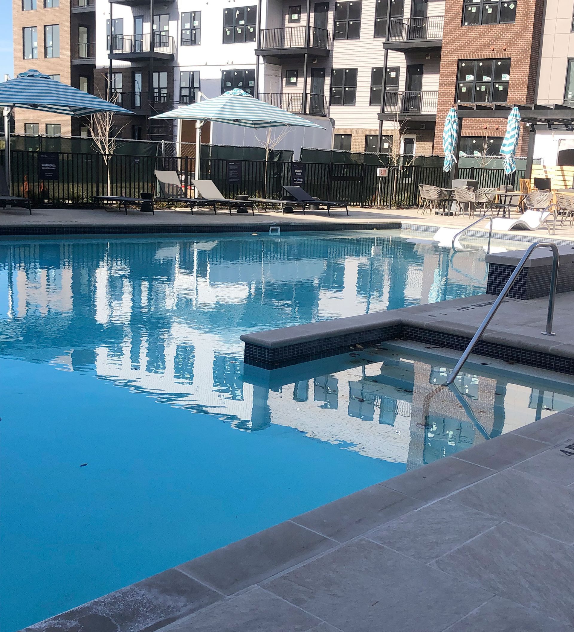 Pool with umbrellas, lounge chairs, and building reflection.