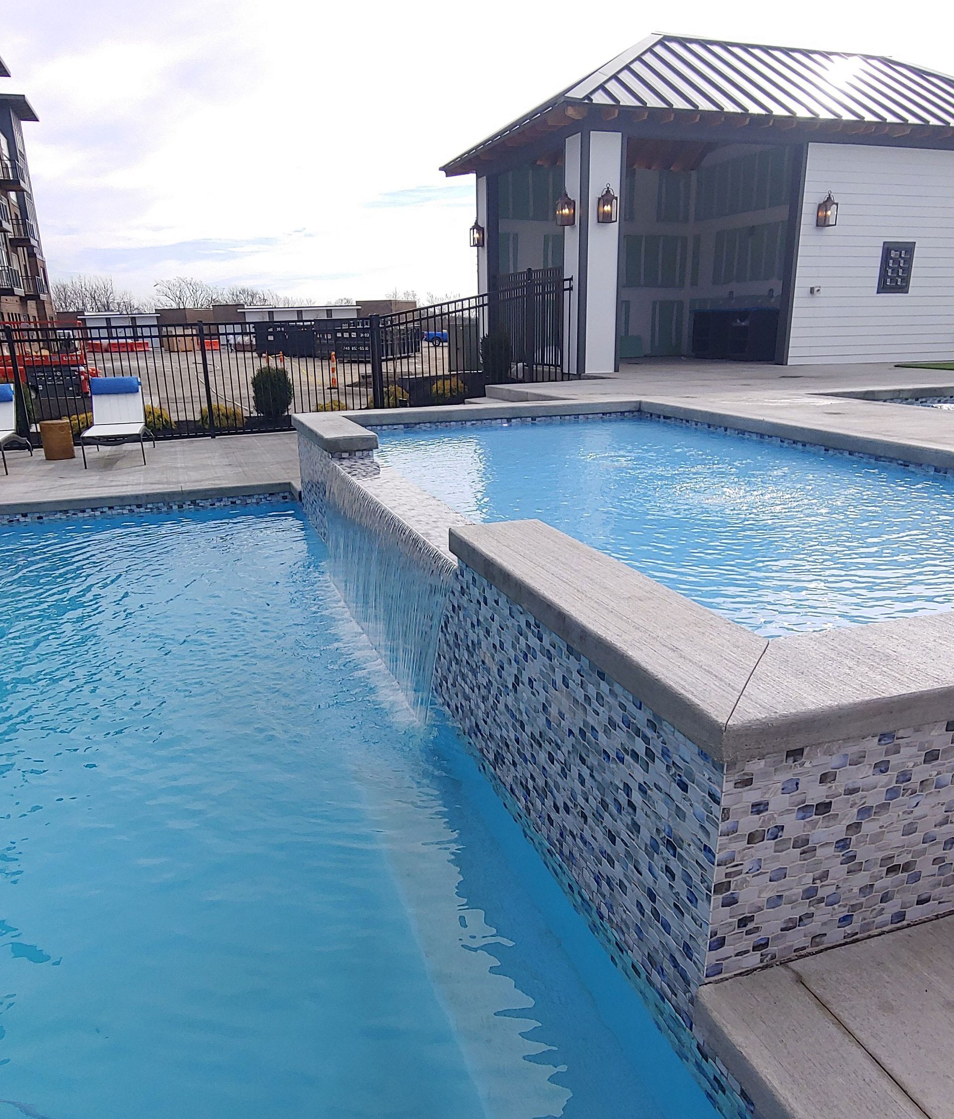 Two blue swimming pools with a tiled wall, near a white building with an overhang.