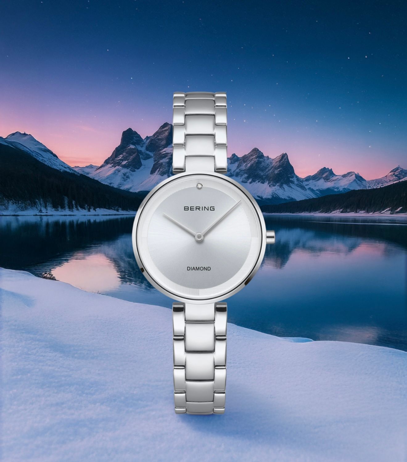 Silver wristwatch with a white face against a snowy landscape and mountains at dusk.
