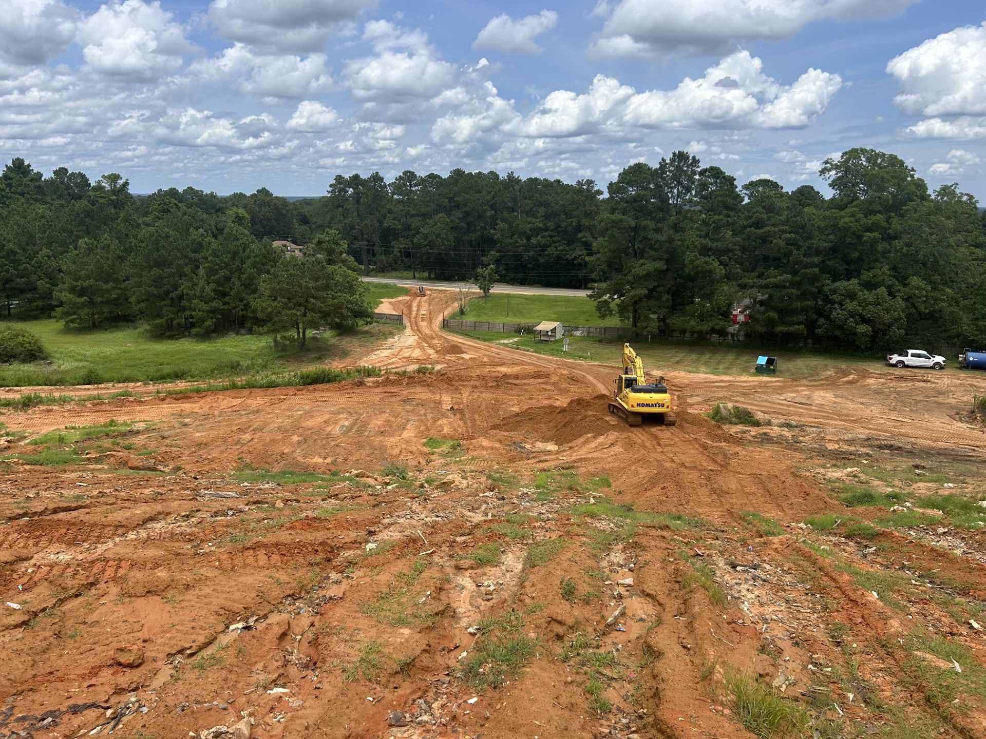 A yellow excavator is working on a dirt road in a field.