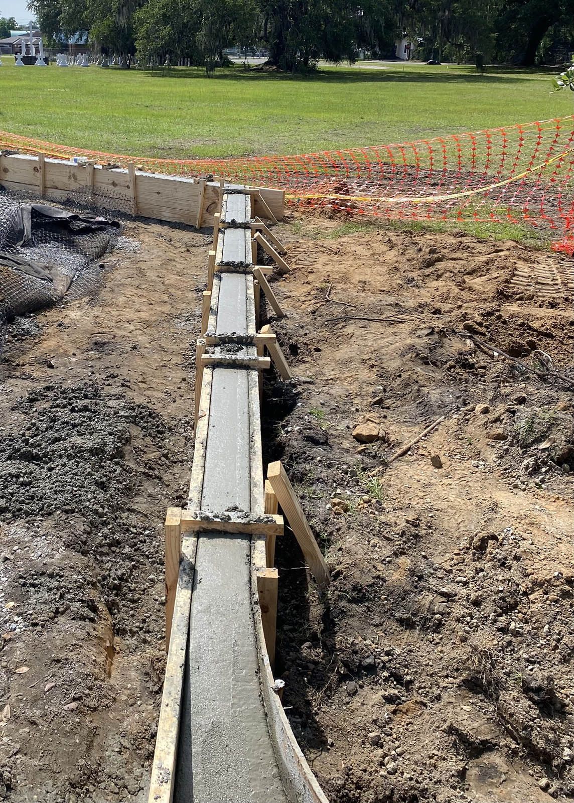 A concrete wall is being built in a field with trees in the background.