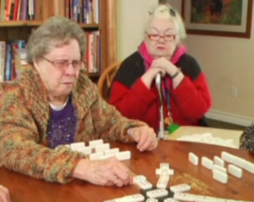 Two elderly women are playing a game of dominoes
