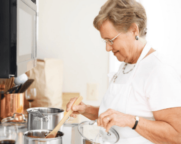 An elderly woman is stirring a pot with a wooden spoon.