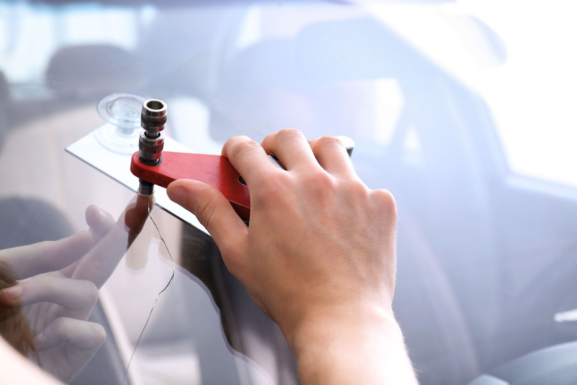 Person repairing a car windshield crack with a red tool.
