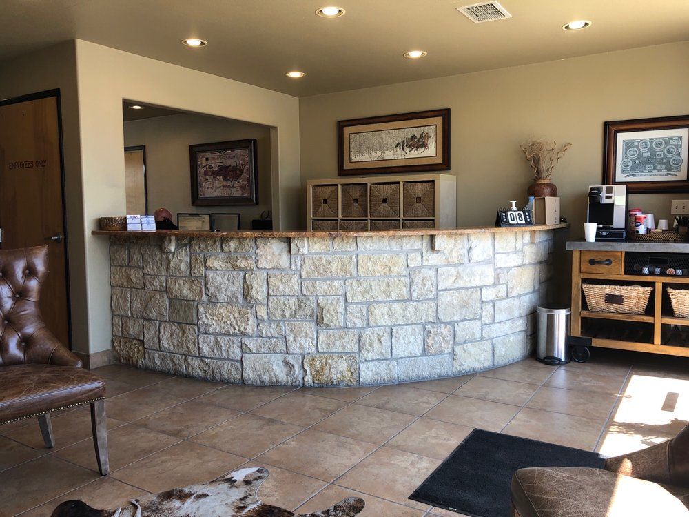 Reception area with stone-faced curved desk, artwork, and coffee station.