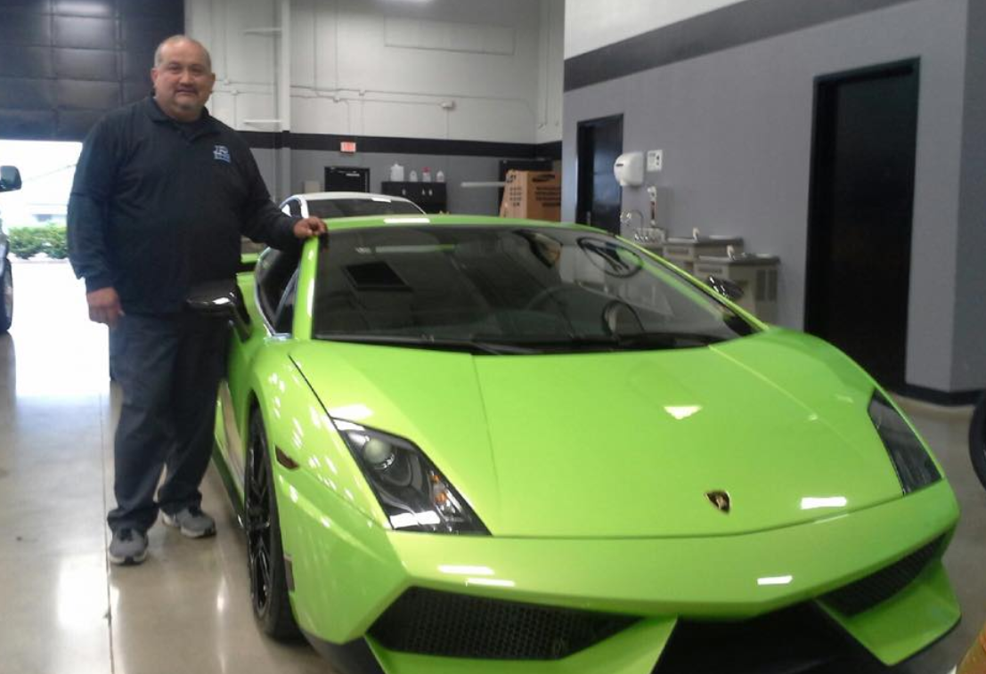 Man in black shirt stands next to a bright green Lamborghini in a garage.