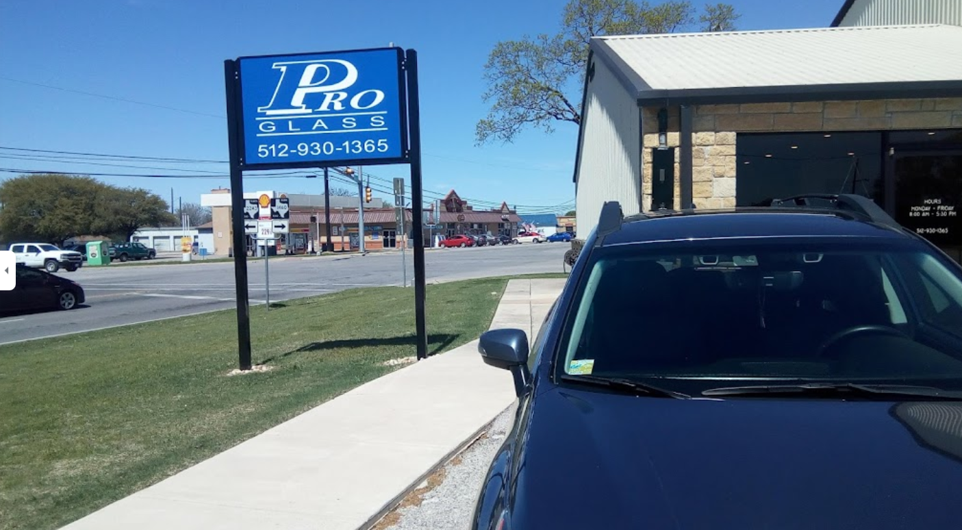Sign for Pro Black with phone number, a blue SUV parked in front on a sunny day.