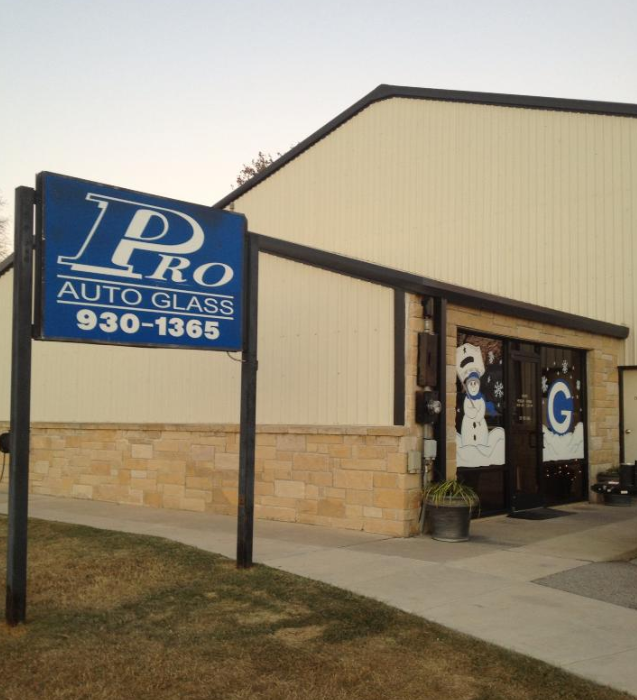 Blue sign for Pro Auto Glass with phone number, in front of a tan building.