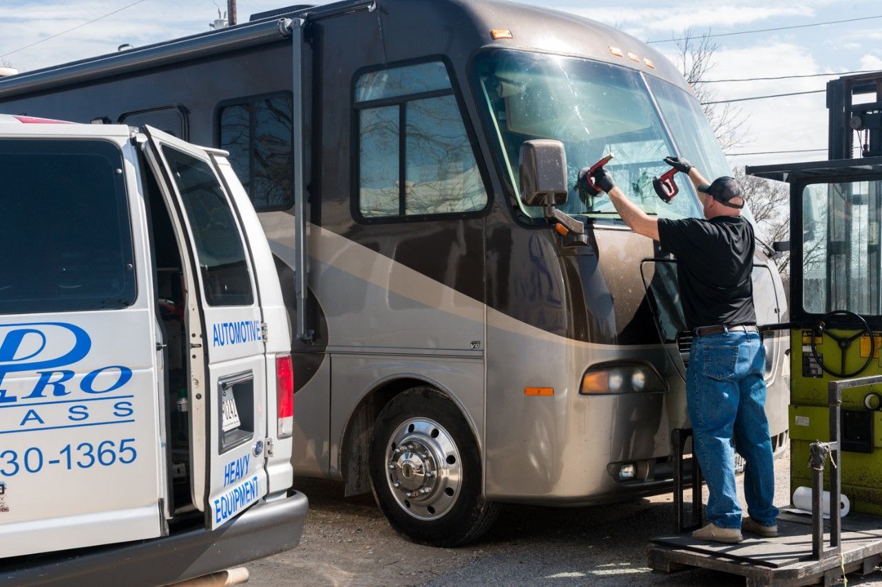 Man washing the windshield of a large RV; white van with company logo visible nearby.