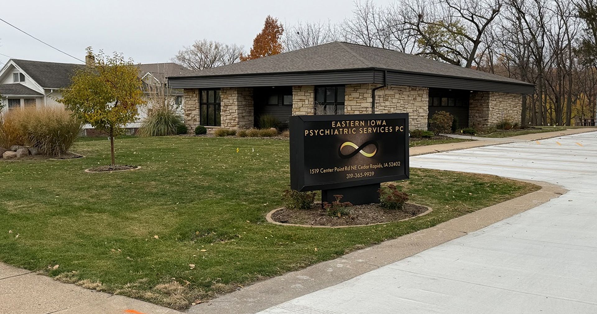 Sign for a business with a light brick building, next to a house, on a cloudy day.