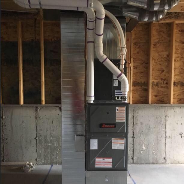 Furnace in a basement with silver ductwork, wooden framing, and concrete walls.