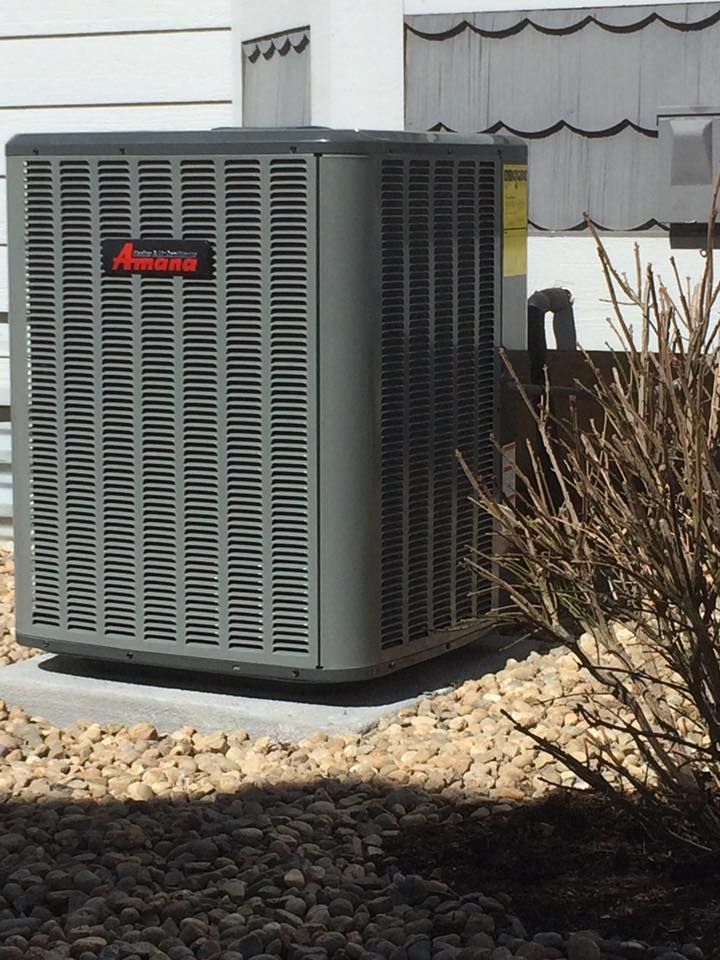 Gray Amana air conditioning unit on a gravel bed near a building.