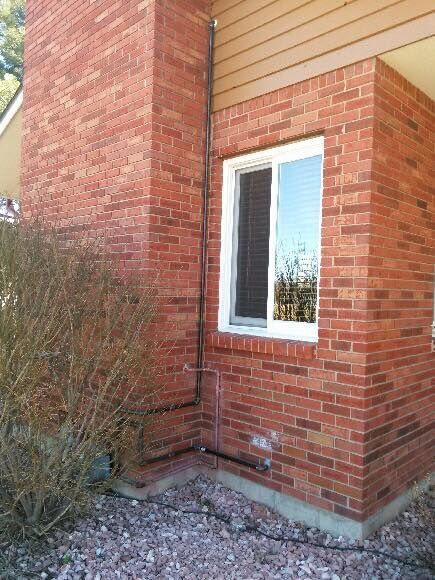 Brick exterior of a building with a window and a chimney. A bush sits at the building's base.