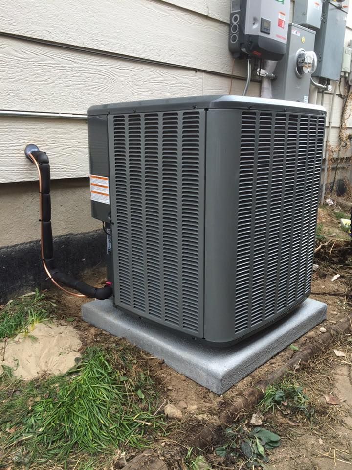 Gray air conditioning unit on concrete base next to a house.