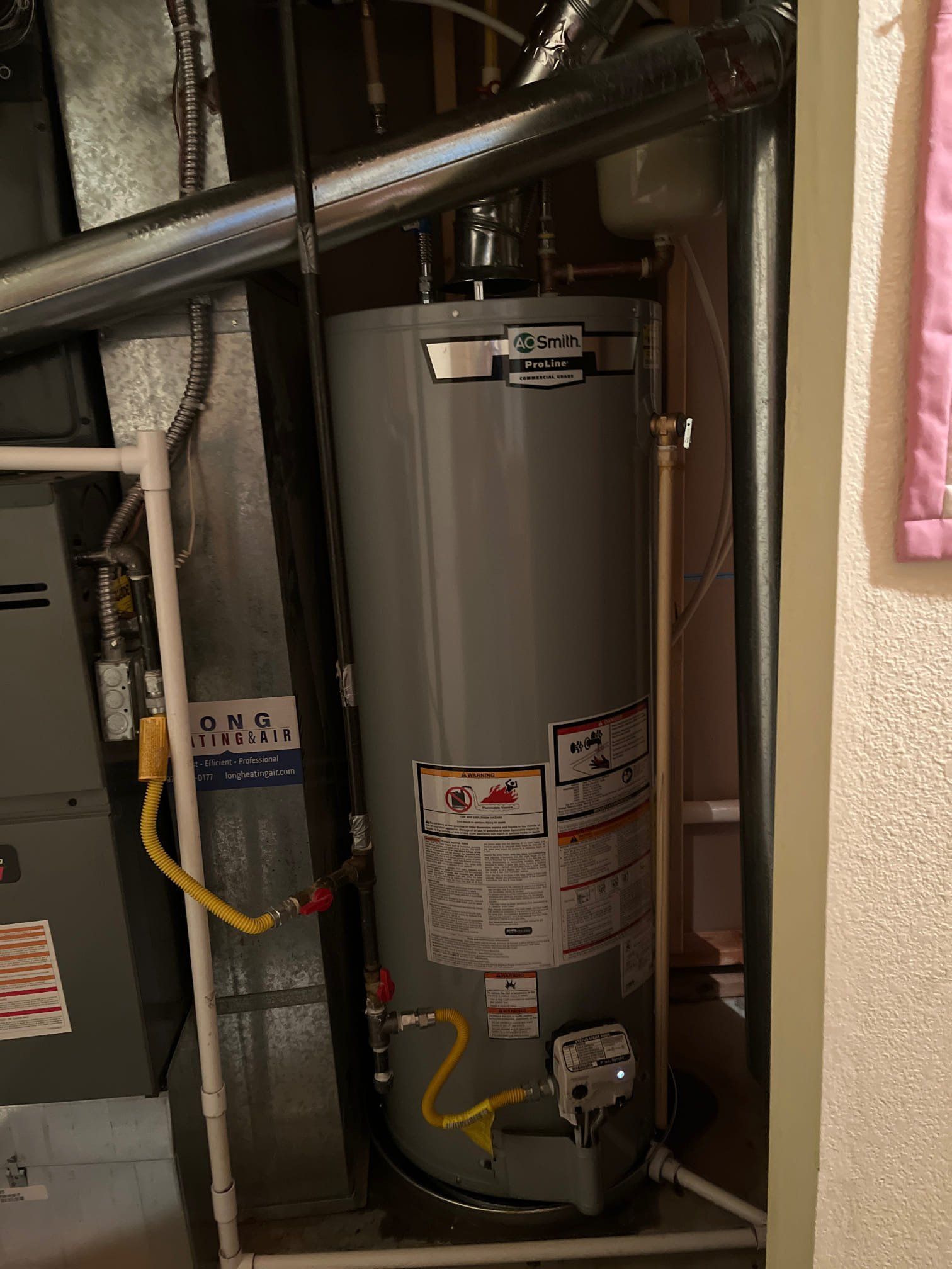 A tall, gray water heater next to ductwork and a furnace in a utility closet.