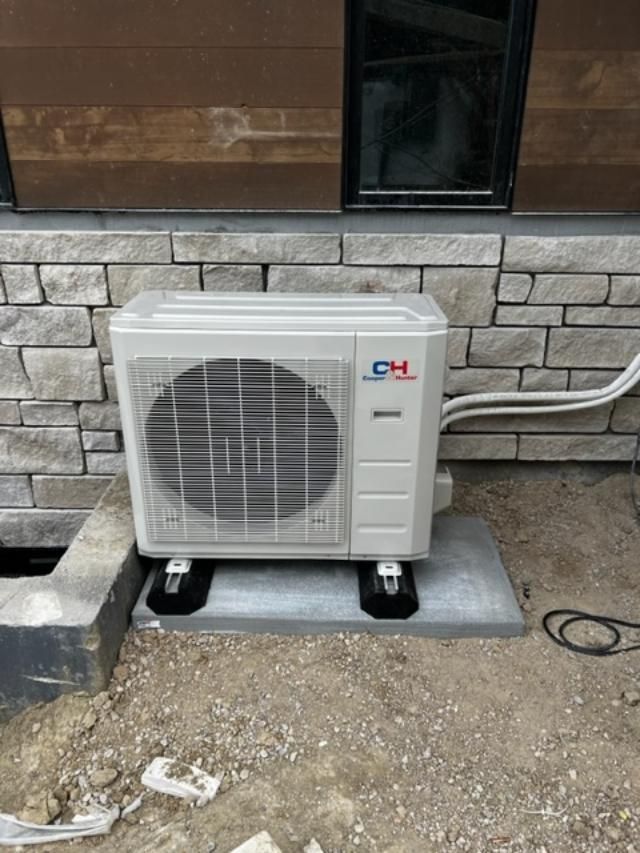 Outdoor air conditioning unit on a concrete pad near a building with stone and wood siding.