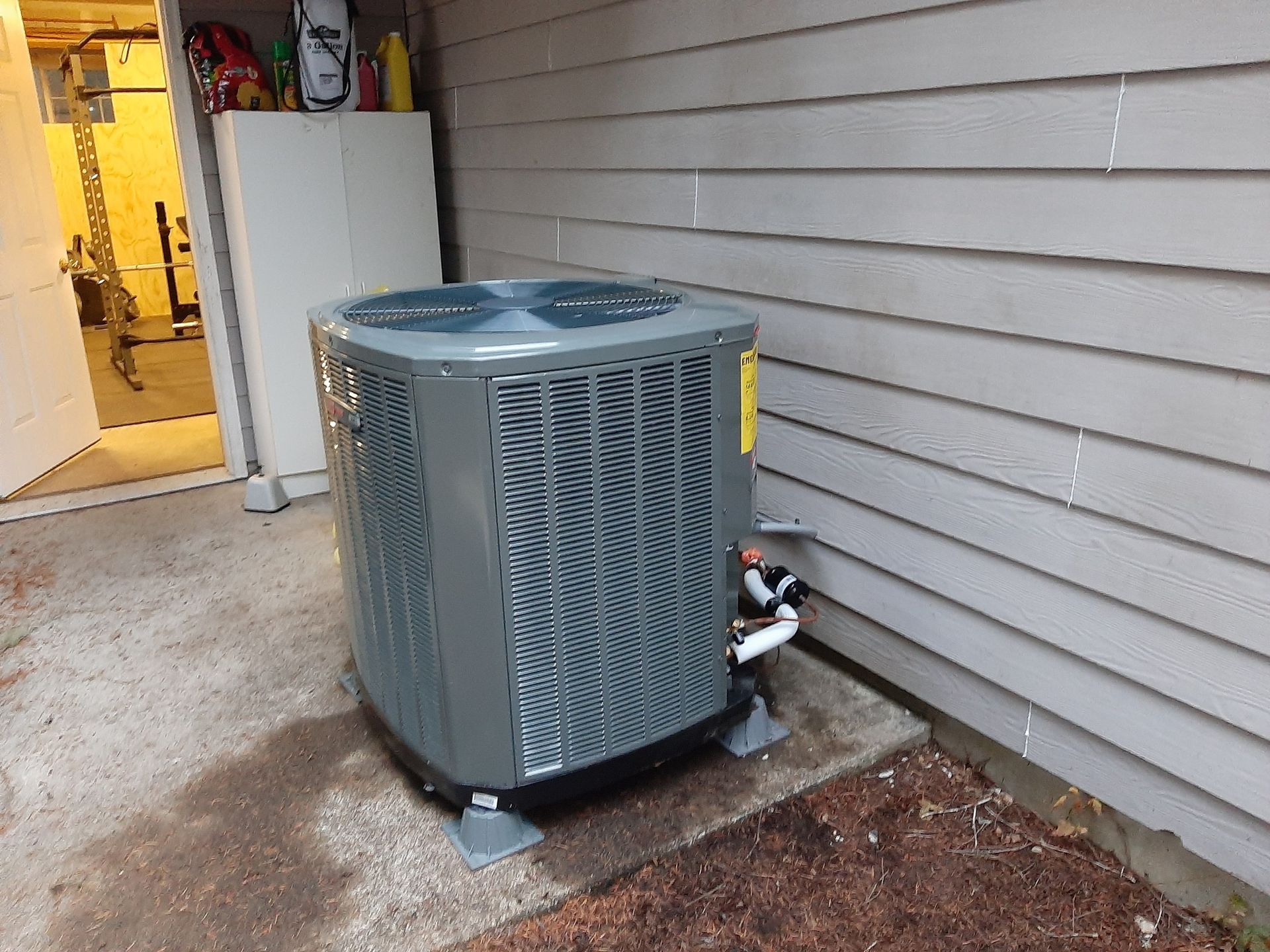 HVAC unit against a gray-sided building; a cabinet and garage entrance visible in background.